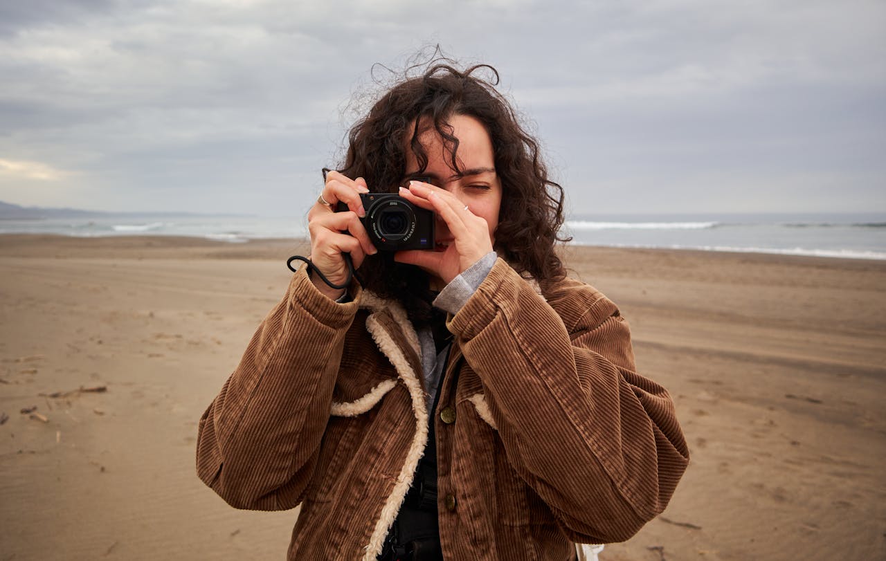 A girl holding a camera, capturing a scenic shot on the beach, surrounded by golden sand and gentle waves, showcasing beach essentials.