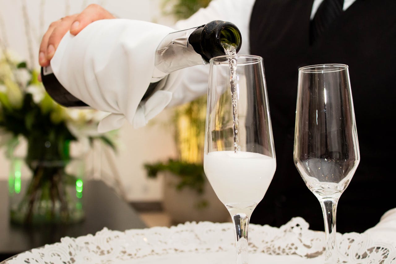 Person pouring champagne into glasses on a well-arranged table, set for a luxurious Valentine's Day 2025 party.