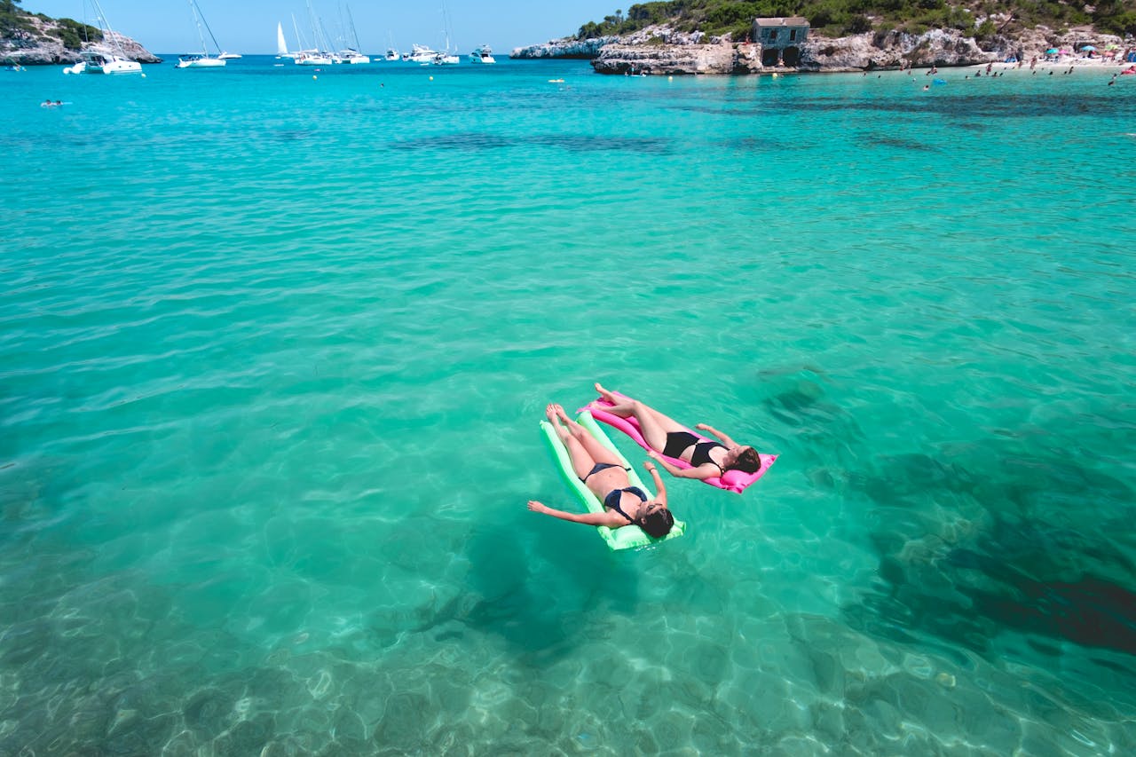 Women relaxing on floating devices in the sun at the beach, enjoying a peaceful day in the water with beach essentials.