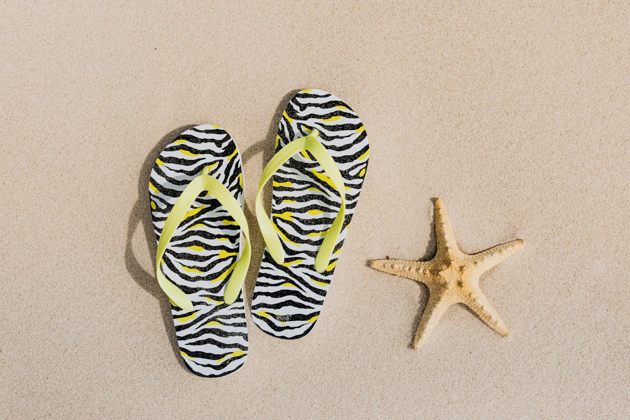 A pair of flip-flops resting on beach sand alongside a starfish, representing beach essentials for a laid-back seaside day.