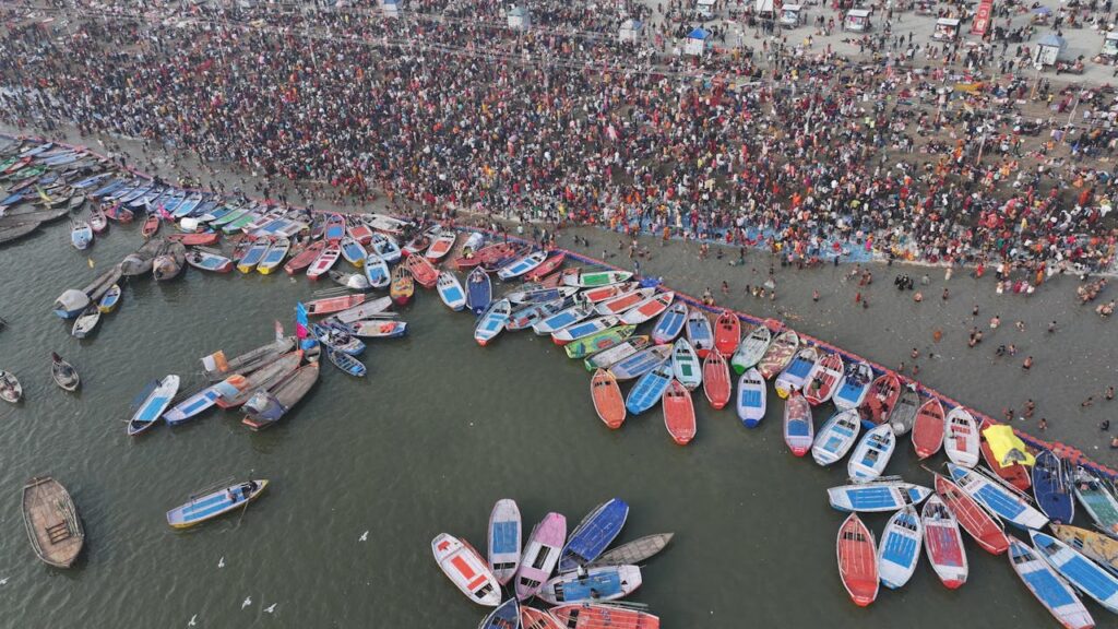 Aerial view of thousands of devotees at Kumbh Mela, immersing in the holy river, with boats providing transportation.