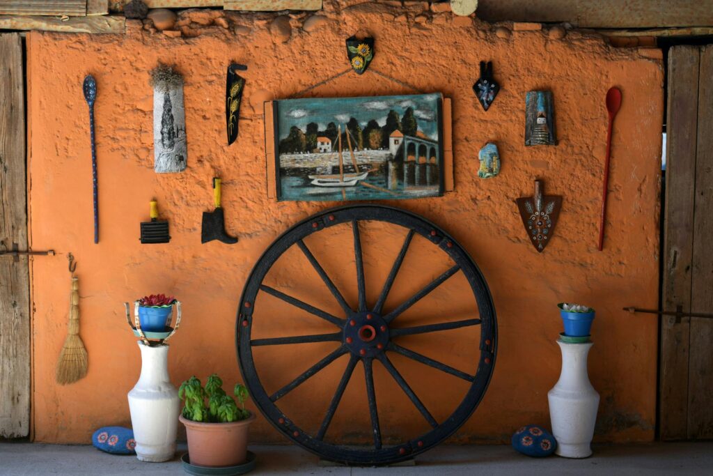 Vintage decor with old items hanging on an orange-colored wall, featuring an old decorated wheel along the wall and a framed photo hanging for added charm.