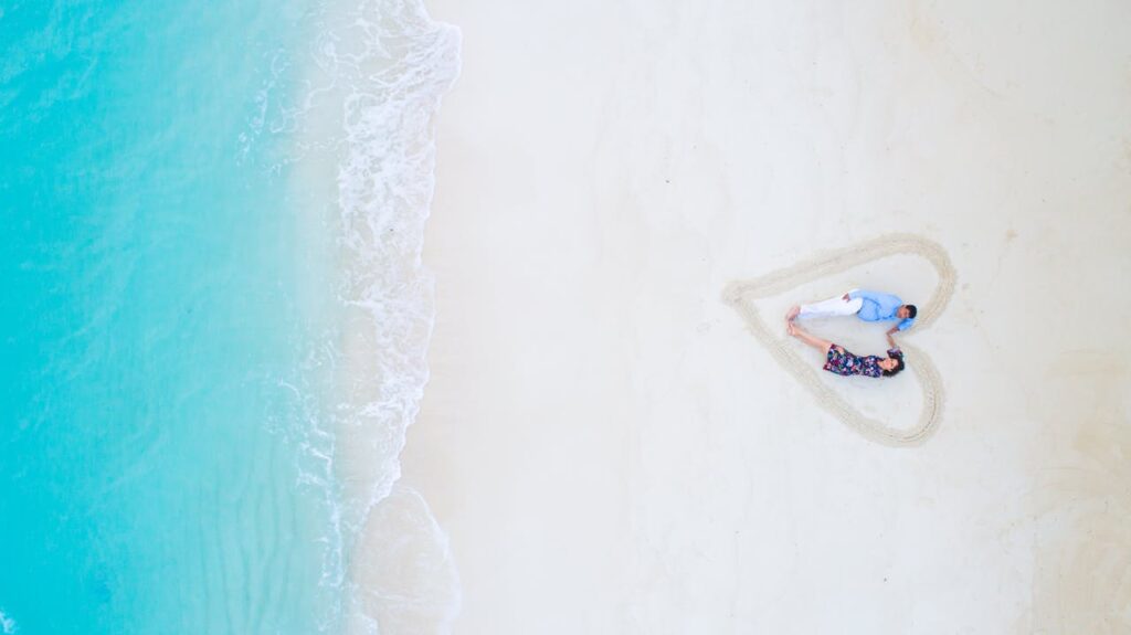 A romantic couple enjoys a special moment in a heart-shaped area on a Maldives beach, surrounded by turquoise waters, celebrating Valentine’s Day on a luxurious romantic escape.