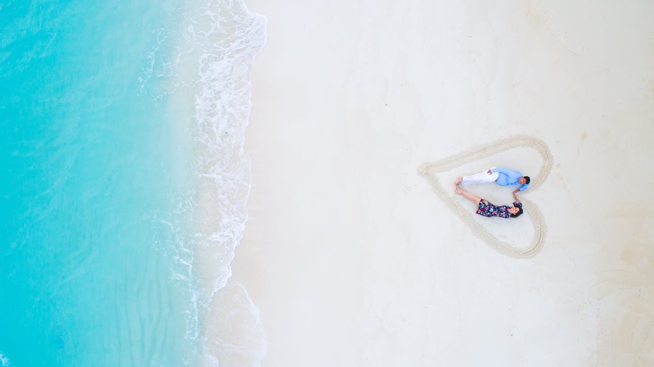 A romantic couple enjoys a special moment in a heart-shaped area on a Maldives beach, surrounded by turquoise waters, celebrating Valentine’s Day 2025 on a luxurious romantic escape.