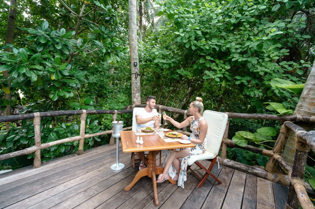 A couple enjoying food and drinks in a beautifully decorated treehouse. How many days until Valentine's Day? Plan a unique and romantic escape in nature.