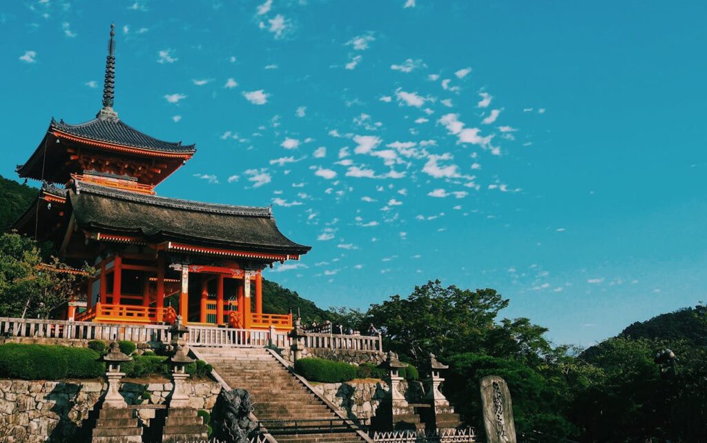 A stunning view of a red and black temple in Kyoto, Japan, surrounded by lush hills, trees, and traditional rock sculptures, creating a serene and romantic atmosphere for a Valentine’s Day 2025 escape.