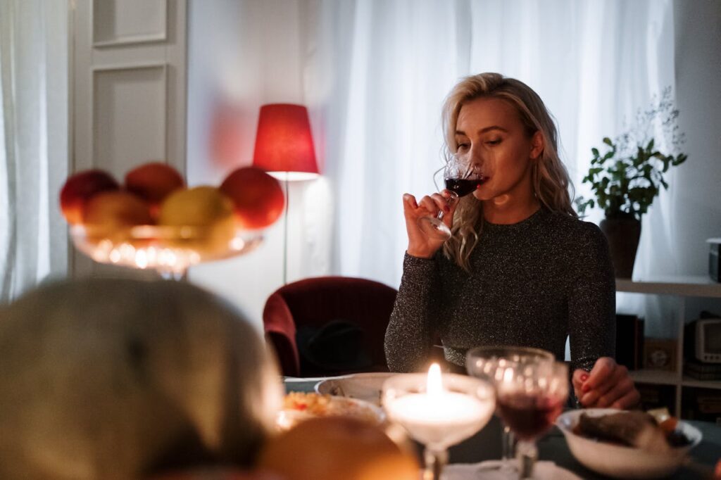 A woman in a restaurant, savoring wine and delicious food, surrounded by candlelight, plants, and fresh fruits on Valentine’s Day for Singles.