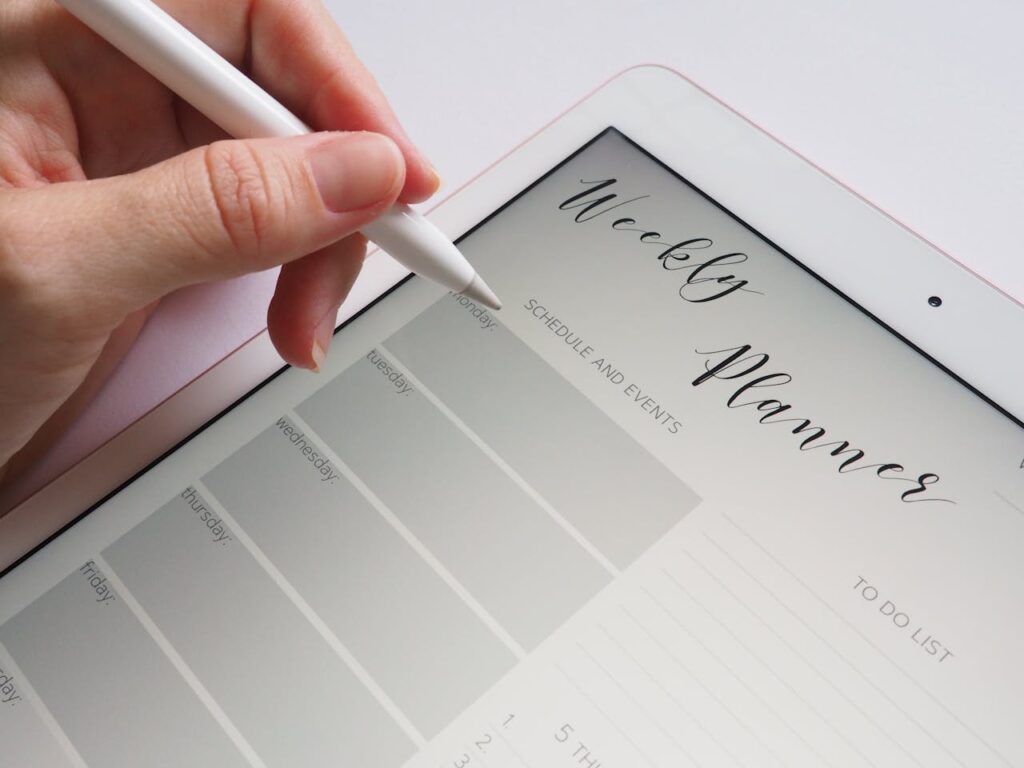 A professional woman's hand writing her schedule in a weekly planner, organizing tasks for efficient business travel and work management.