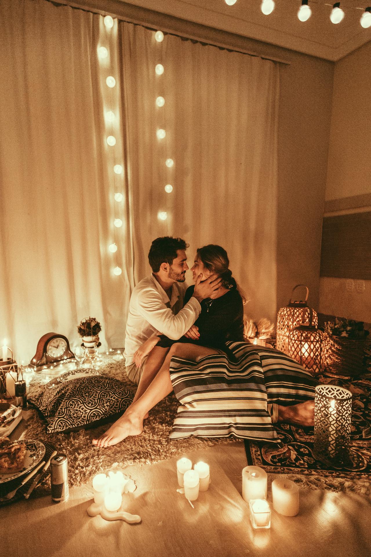 A couple sitting together in a cozy room, enjoying intimate moments with warm yellow lights, candles, and soft cushions during Valentine's Week 2025.