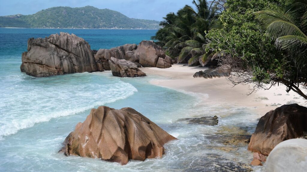 A breathtaking beach view in Seychelles, featuring pristine white sand, turquoise waters, lush trees, and stunning large rock formations, creating a perfect romantic escape for Valentine’s Day 2025.