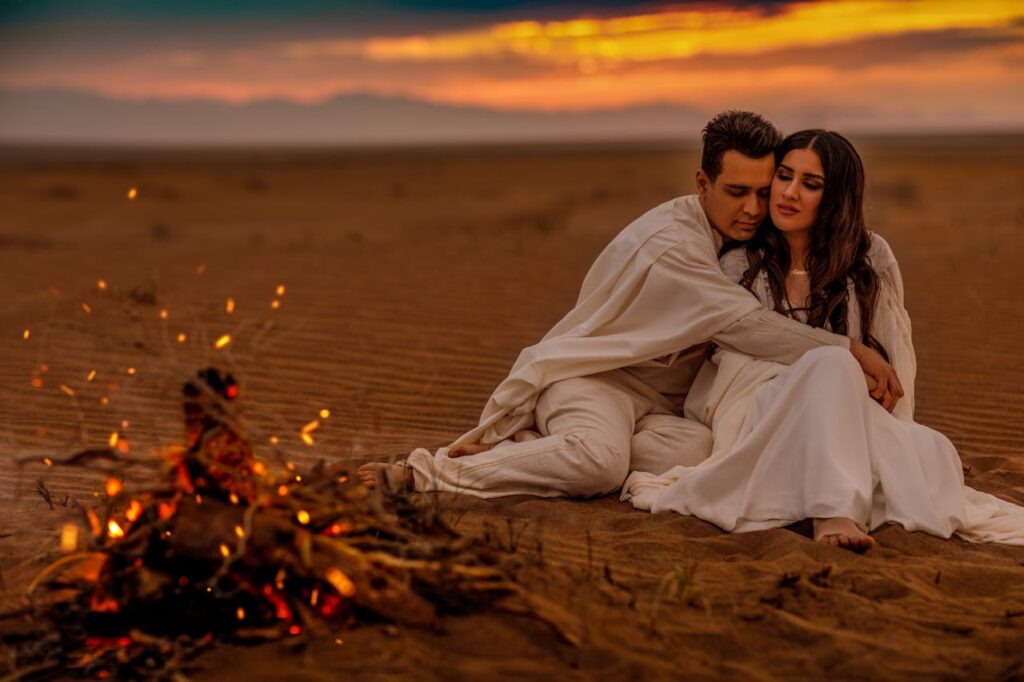 A romantic couple enjoys a private moment in the Dubai desert, with a glowing bonfire nearby, under the evening sky, creating a magical Valentine’s Day 2025 escape.