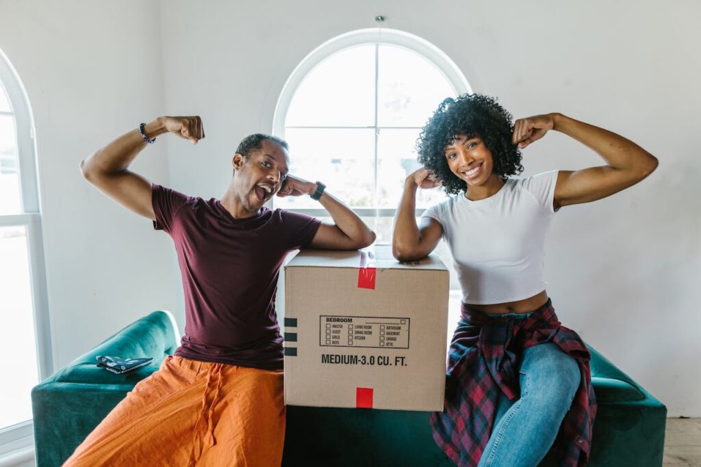 New Airbnb hosts preparing their rental by unpacking and setting up the space, a key step in how to become an Airbnb host. They sit on the couch, smiling and motivated for their hosting journey.