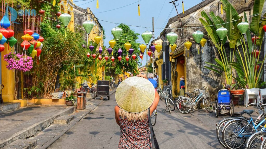 A woman wearing a hat takes a photo of a beautifully decorated street with bicycles in Vietnam during her Vietnam travel itinerary.