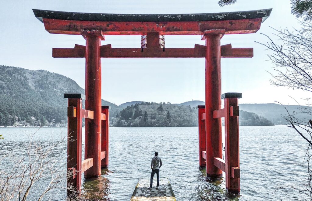 Man in gray jacket standing on a dock in Hakone, Japan, admiring torii gates by the lake, a peaceful moment in a Japan travel itinerary.