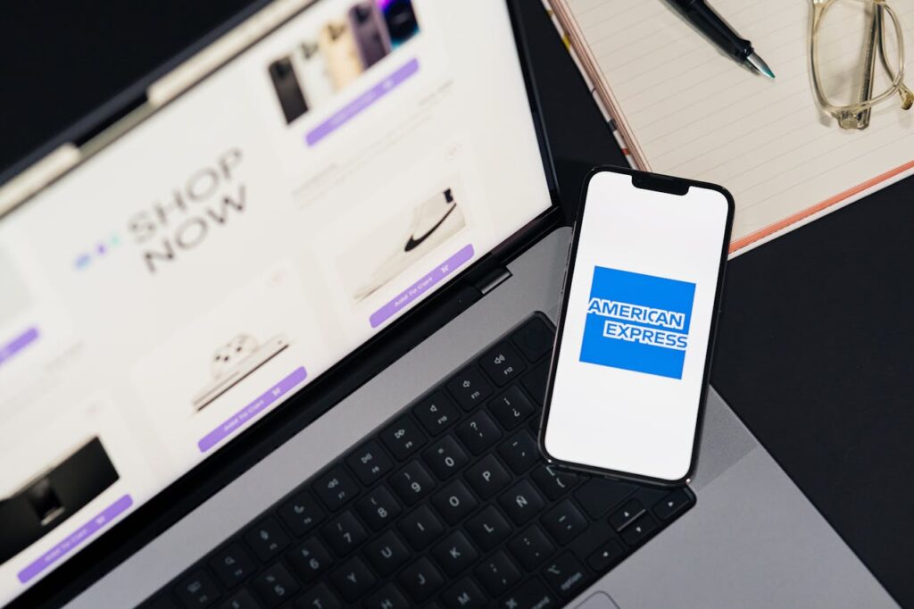 Mobile with American Express app and laptop showing shopping site on table—powered by American Express Corporate Travel