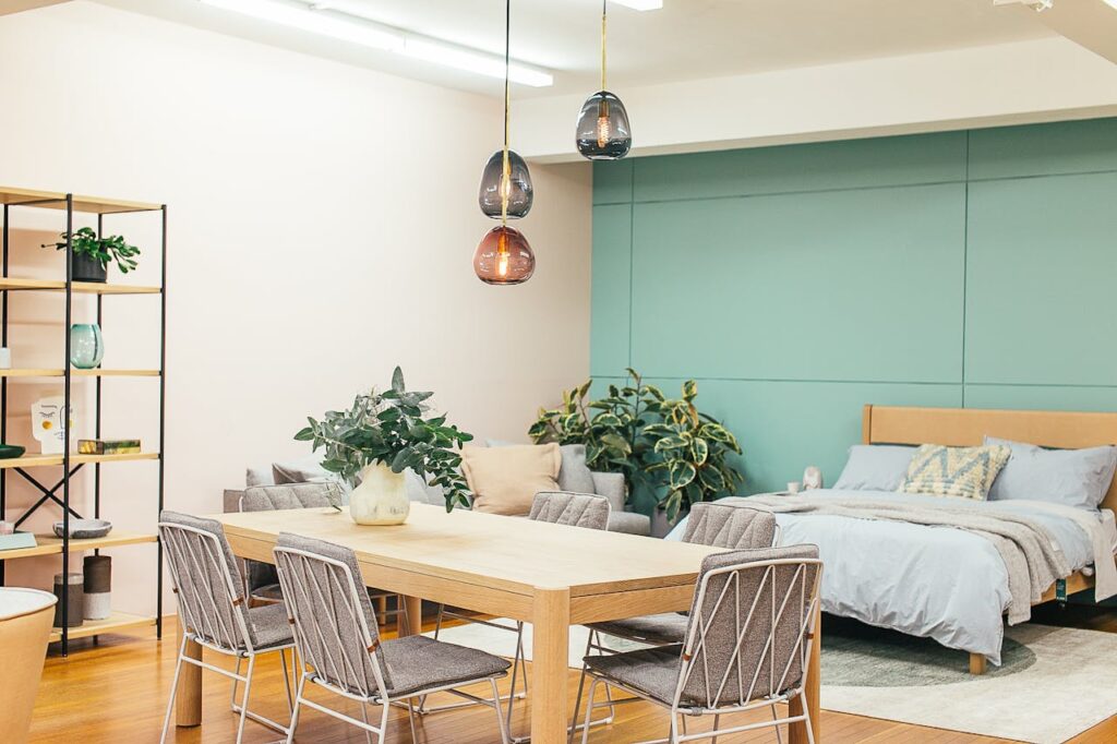 A nature-themed bedroom with indoor plants, green wall paint, adjoining dining area, and elegant ceiling lamps, styled with Westside Home Decor.