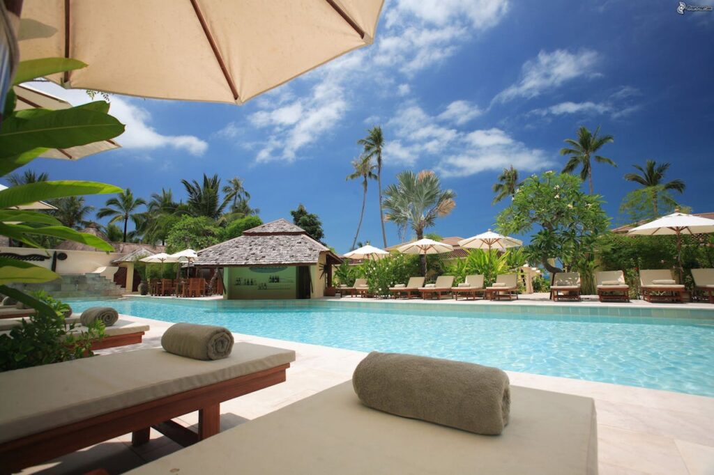 Outdoor resort swimming pool with coconut trees and sitting area, promoting safe swimming practices to prevent brain eating amoeba risks.